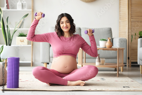 Sporty pregnant woman training with dumbbells at home photo
