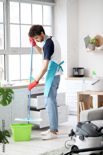 Young man mopping floor in kitchen