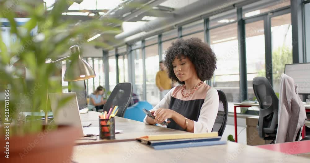 African american woman using smartphone sitting on her desk at office