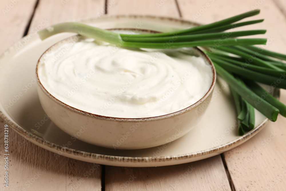 Bowl of tasty sour cream with green onion on light wooden background Bowl of tasty sour cream with green onion on light wooden background