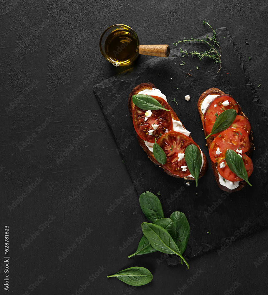 Delicious toasted bread with tomatoes, feta cheese, spinach and herbs on black board, close up, copy space Delicious toasted bread with tomatoes, feta cheese, spinach and herbs on black board, close up, copy space