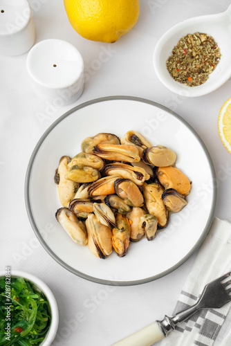 Plate with pickled mussels and bowl of seaweed salad on white background