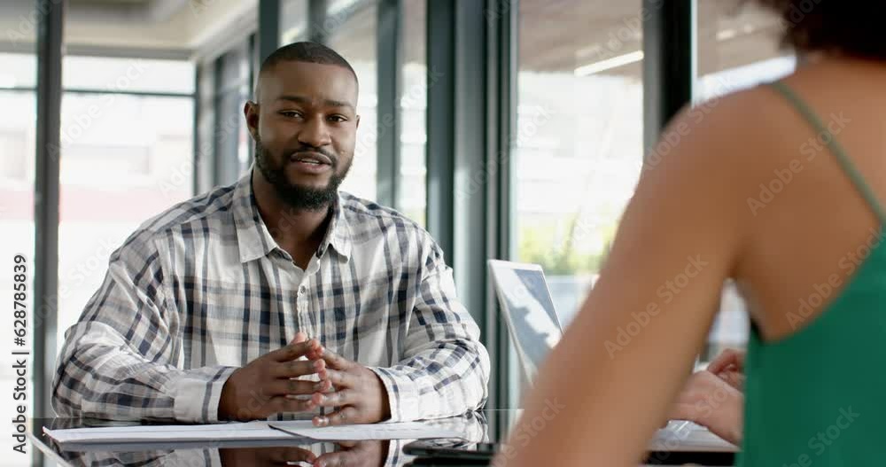 Three diverse colleagues discussing while sitting on a table together at office Three diverse colleagues discussing while sitting on a table together at office