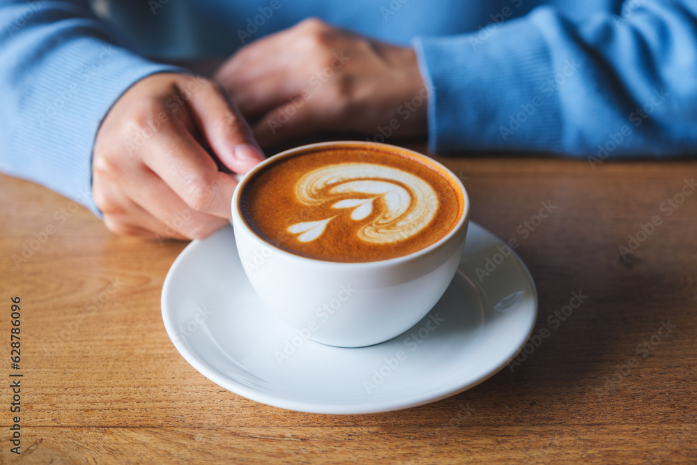 Closeup image of a woman holding a cup of latte coffee on wooden table Closeup image of a woman holding a cup of latte coffee on wooden table