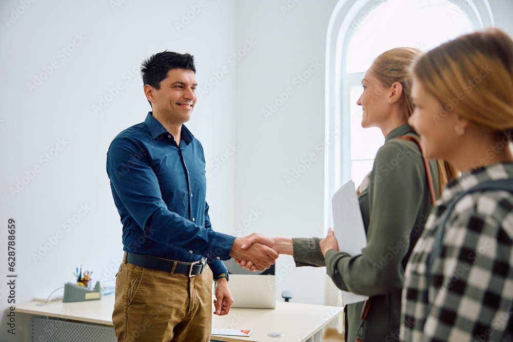 Happy principal shaking hands with mother who has come for her daughter's enrollment in high school. Happy principal shaking hands with mother who has come for her daughter's enrollment in high school.