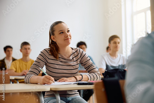 Smiling female student taking notes during class at high school.