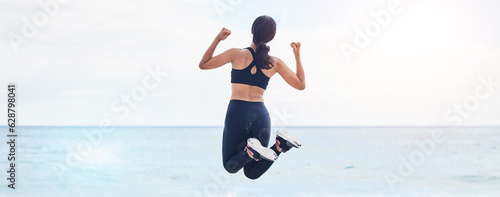 Back  freedom and fitness woman jump at the beach with celebration after running  training or workout success in nature. Exercise  jumping and behind female at the sea celebrating goal milestone