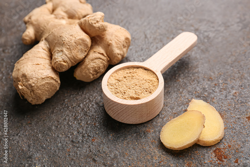 Fresh ginger root and wooden spoon with dried powder on dark background