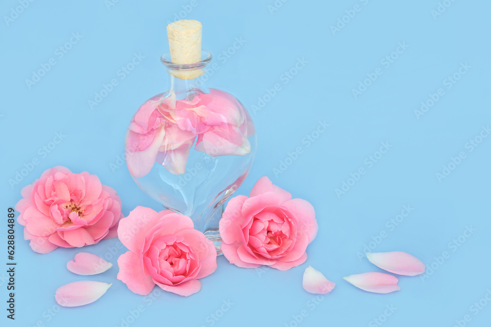 Rosewater for natural skincare in heart shaped bottle with pink rose flowers and petals on blue. Can balance ph of skin oils, reduce redness, naturally hydrates skin. Rosewater for natural skincare in heart shaped bottle with pink rose flowers and petals on blue. Can balance ph of skin oils, reduce redness, naturally hydrates skin.