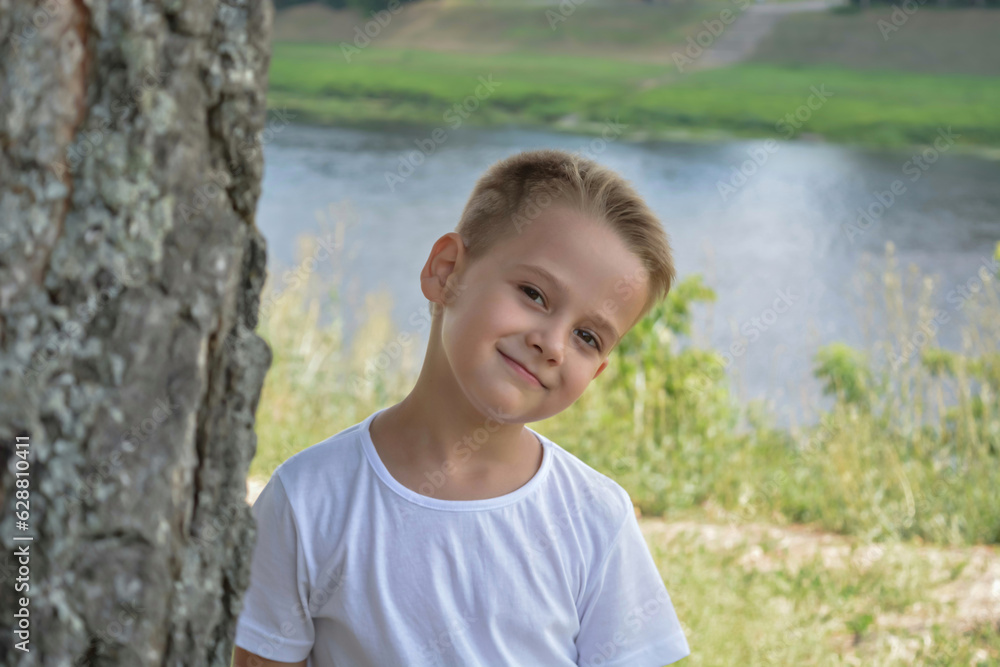 a cute boy in the park looks out from behind a tree and smiles a cute boy in the park looks out from behind a tree and smiles