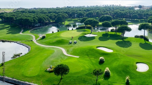 Top view of two men playing golf on a sunny summer day. Aerial view of the green golf course. Hitting the ball with a golf stick. An active type of recreation. Golf car