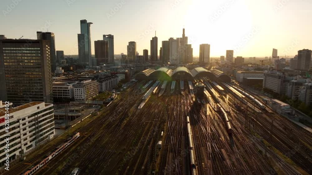 AERIAL: Frontal flight over Frankfurt am Main early morning in yellow-brown range. Central train station Germany, train tracks with low traffic. High angle view of the station building.