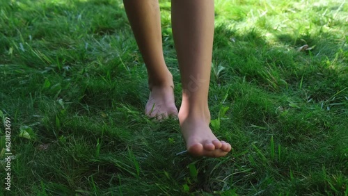 legs of a teenage girl barefoot walking towards the camera, stepping on green grass or lawn, front view