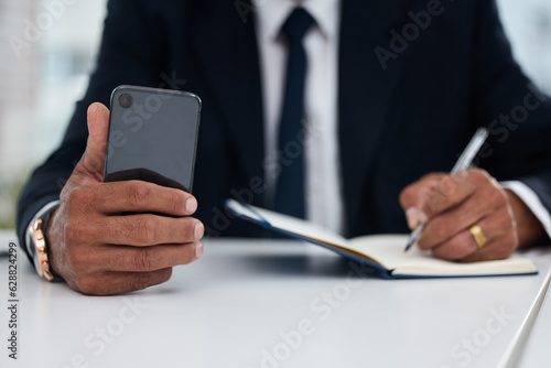 Table, hands and businessman with phone and notebook for planning, schedule or work agenda. Office, writing and a corporate employee with a planner and a mobile for an app while working on a reminder