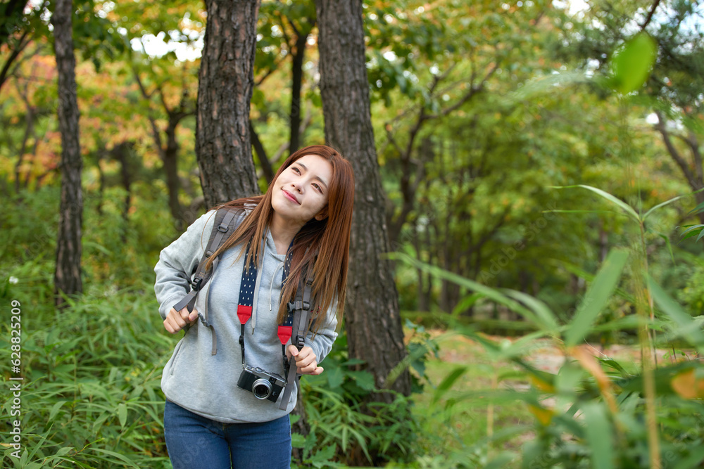 A young woman walking around in the woods taking pictures with a camera and backpack A young woman walking around in the woods taking pictures with a camera and backpack