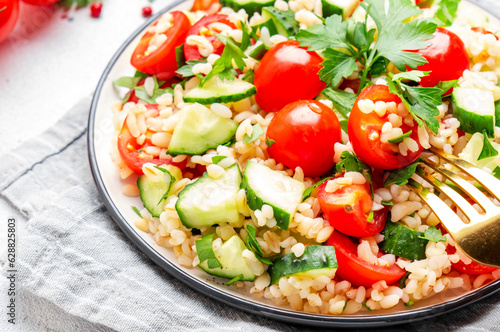 Bulgur tabbouleh salad with tomatoes, cucumbers and parsley. Traditional Middle Eastern dish. White table background, top view