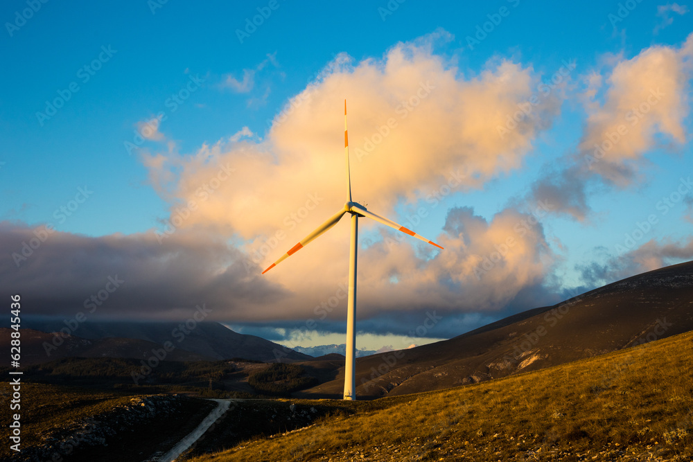 Conceptual photo background of tranquility at sunset. A wind farm with wind turbines in the mountains with snow and clouds. Calm sunset light and for wallpapers on your computer or phone