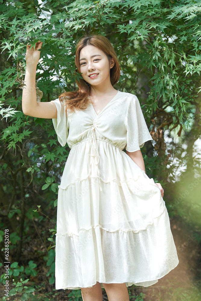 In summer daytime, a beautiful Asian woman wearing a dress in a forested park is doing various movements. In summer daytime, a beautiful Asian woman wearing a dress in a forested park is doing various movements.