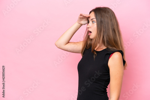 Young caucasian woman isolated on pink background with surprise expression while looking side