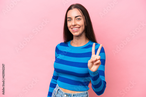 Young caucasian woman isolated on pink background smiling and showing victory sign