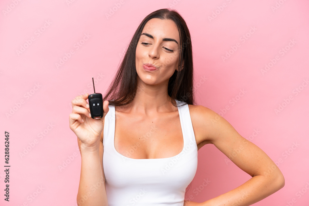 Young caucasian woman holding car keys isolated on pink background with sad expression Young caucasian woman holding car keys isolated on pink background with sad expression