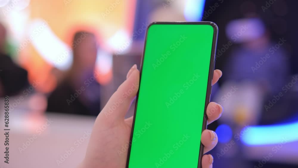 Handheld Camera: back view of brunette holding chroma key green screen smartphone watching content. Shopping online. Gadgets and contemporary people concept. Handheld Camera: back view of brunette holding chroma key green screen smartphone watching content. Shopping online. Gadgets and contemporary people concept.