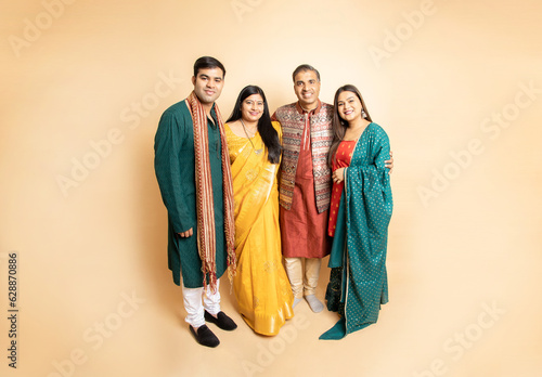 Happy indian family wearing traditional cloths standing isolated on beige background. Celebrating diwali festival, Occasion of wedding, Ethnic wear fashion.