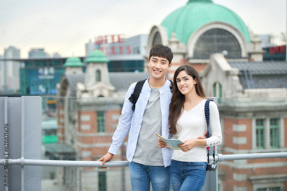 During the trip, a college student couple is looking for their way with a map at Seoul Station during the day.