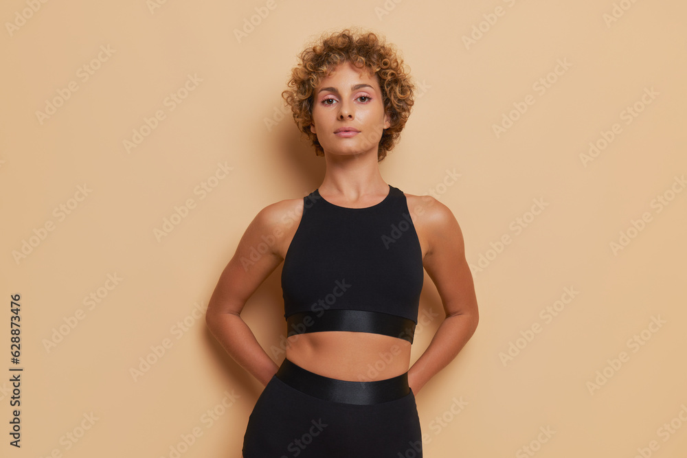 Graceful woman with curly short hair in black top stands isolated on ...