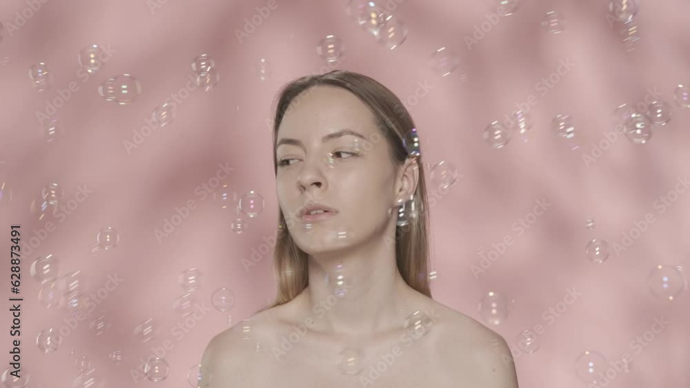 A woman with naked shoulders in the studio surrounded by soap bubbles on a pink background. A woman watches soap bubbles. Slow motion. HDR BT2020 HLG Material. A woman with naked shoulders in the studio surrounded by soap bubbles on a pink background. A woman watches soap bubbles. Slow motion. HDR BT2020 HLG Material.
