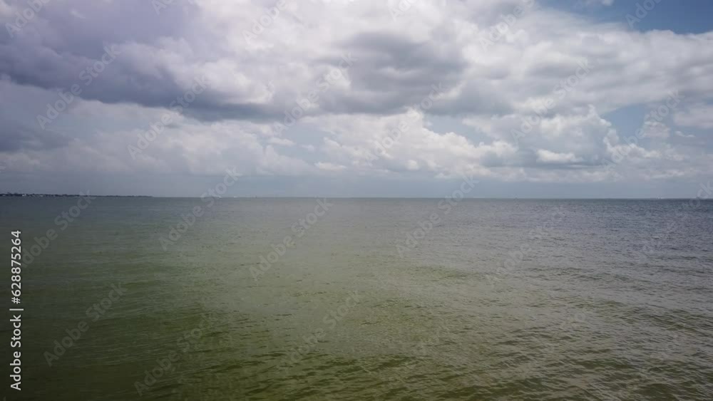 View looking east from south St. Petersburg, FL towards Tampa bay with small boat in background. Sunny day with white puffy clouds and blue sky. Waters are calm View looking east from south St. Petersburg, FL towards Tampa bay with small boat in background. Sunny day with white puffy clouds and blue sky. Waters are calm