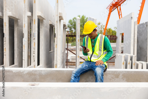 Happy worker enjoying free time and using smartphone. Asian man forman warehouse worker sitting on workshop site break relax time at Heavy Industry Manufacturing Prefabricated concrete walls Factory