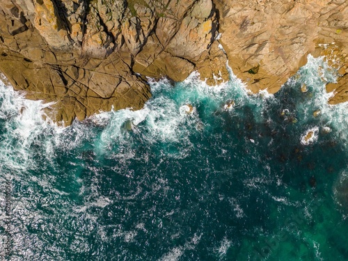 Bild auf Leinwand Aerial view of ocean waves crashing against the coastline on a sunny day