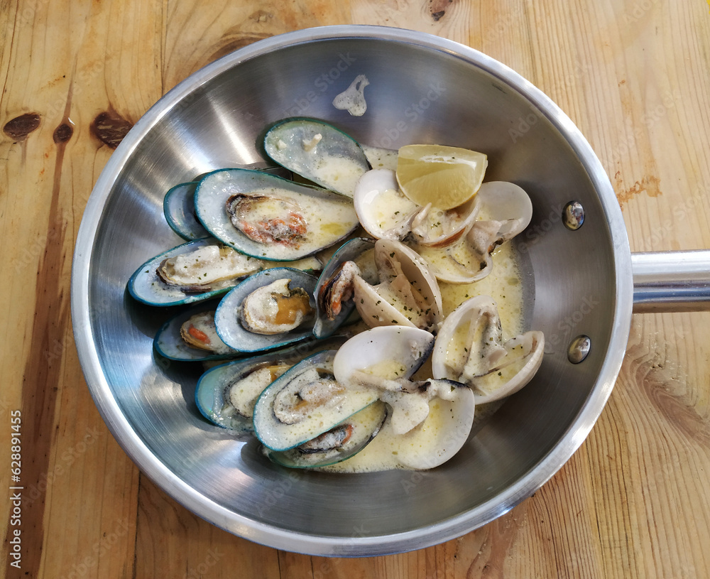 Mussels Clams Kiwi in cheese sauce in cooking pan on wooden background Mussels Clams Kiwi in cheese sauce in cooking pan on wooden background