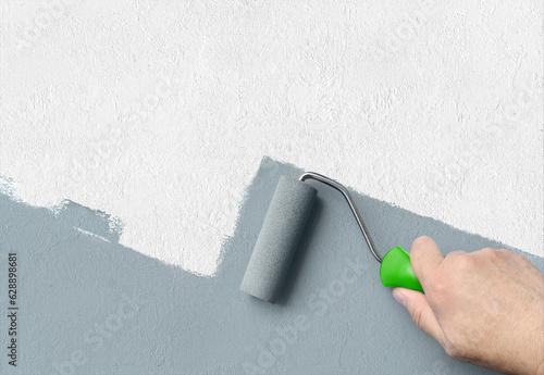 Man applying grey paint with roller brush on white wall, copy space