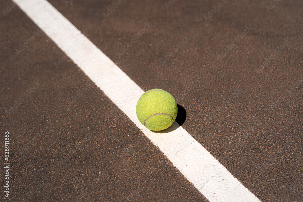 Yellow tennis ball placed on white mark on sports ground in sunlight