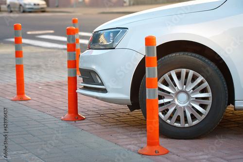 Car parked close to warning post at parking lot. Car parked close to flexible orange traffic reflective bollard. Plastic parking barrier, prevent car parking on pedestrian area. photo