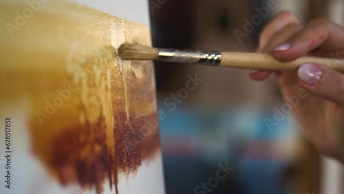 Female hand painting with brush acrylic or oil paint on canvas. Artist paints an oil painting in the studio, close-up, creator creates a work of art
