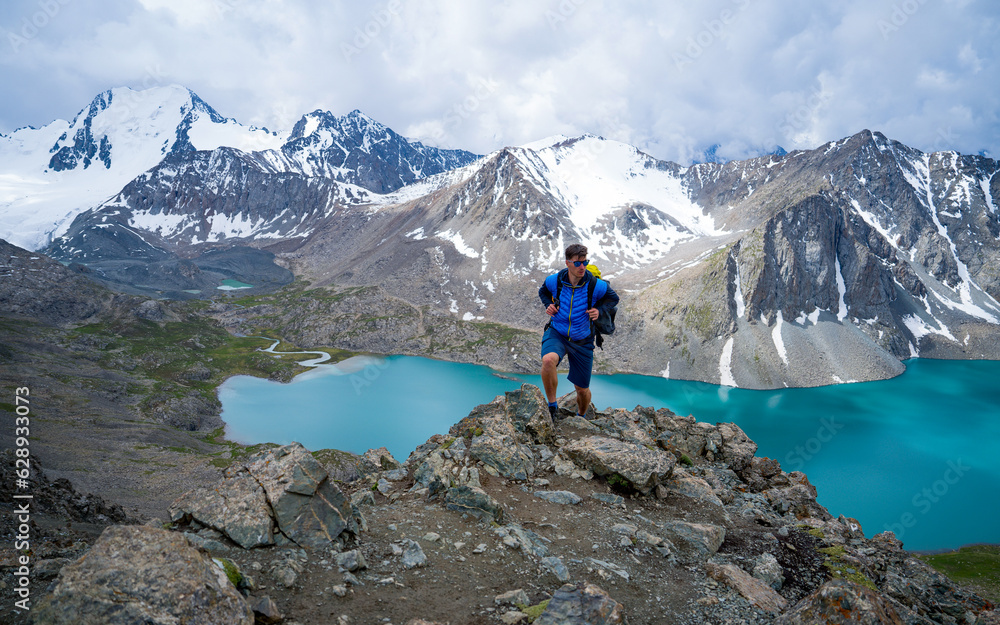 Traveler on the mountain peak, overlooking the lake and mountains. Exploring the concept of travel, adventure, or expedition. Ala Kul lake,  Kyrgyzstan. Sportswear, functional for the mountains.