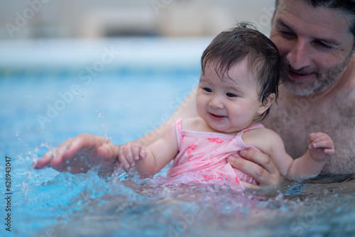 lifestyle portrait of father and little daughter enjoying summer - man holding her sweet baby girl excited and cheerful playing together at resort swimming pool in parenting concept © TheVisualsYouNeed