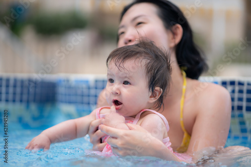happy and beautiful Asian woman holding her little baby girl playful - Korean mother and adorable daughter playing on water at resort swimming pool in Summer © TheVisualsYouNeed