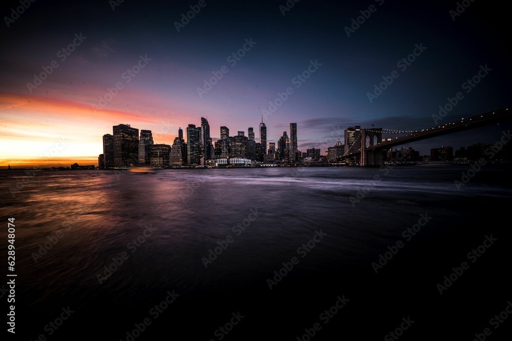Obraz premium Beautiful view of the city of Manhattan during sunset, with the sun casting an orange hue