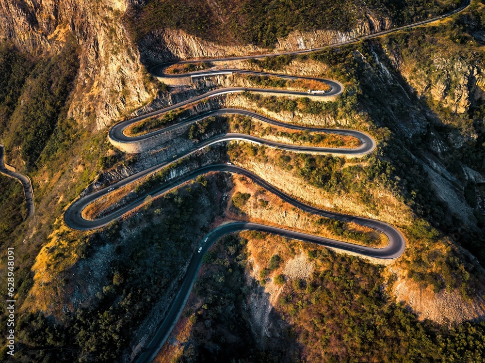 Aerial view of a winding mountain road, showcasing its sharp curves and rugged terrain Aerial view of a winding mountain road, showcasing its sharp curves and rugged terrain