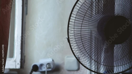A fan standing in a room next to a large window. Fan on and running creates fresh air and comfort