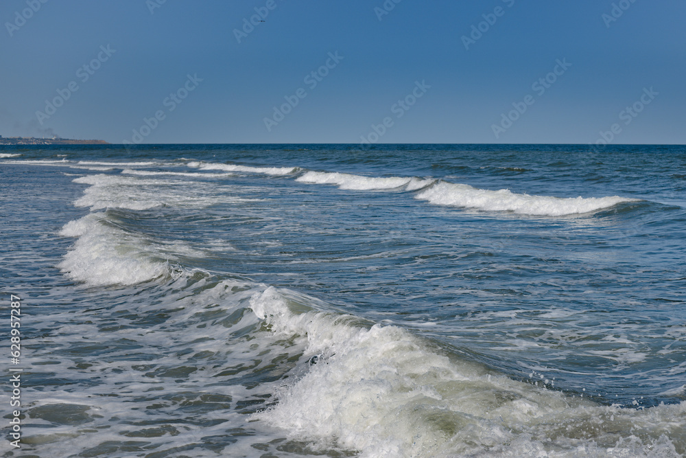 Fototapeta premium Waves rolling on the shore. The blue color of the sky is reflected in the water of the sea.