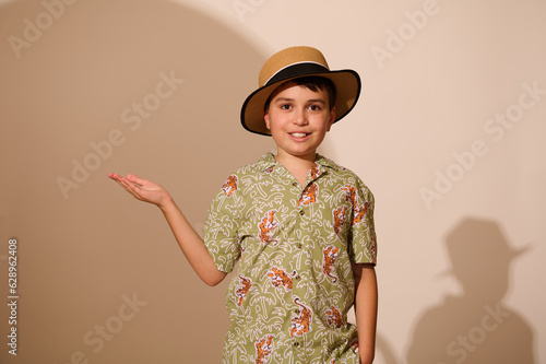 Latin American charming teenage boy tourist traveler in summer clothes, holding imaginary copy ad space on hand palm up