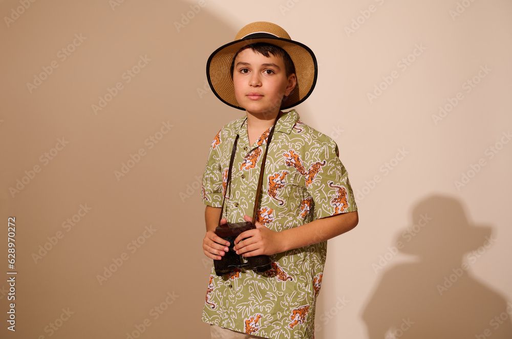 Cute teenage boy, traveler tourist adventurer in summer wear, holding binoculars, looking at camera, isolated background