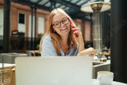 Young smiling Caucasian woman student calling with cell telephone while sitting alone in coffee shop during free time, attractive female with cute smile having talking conversation with mobile phone
