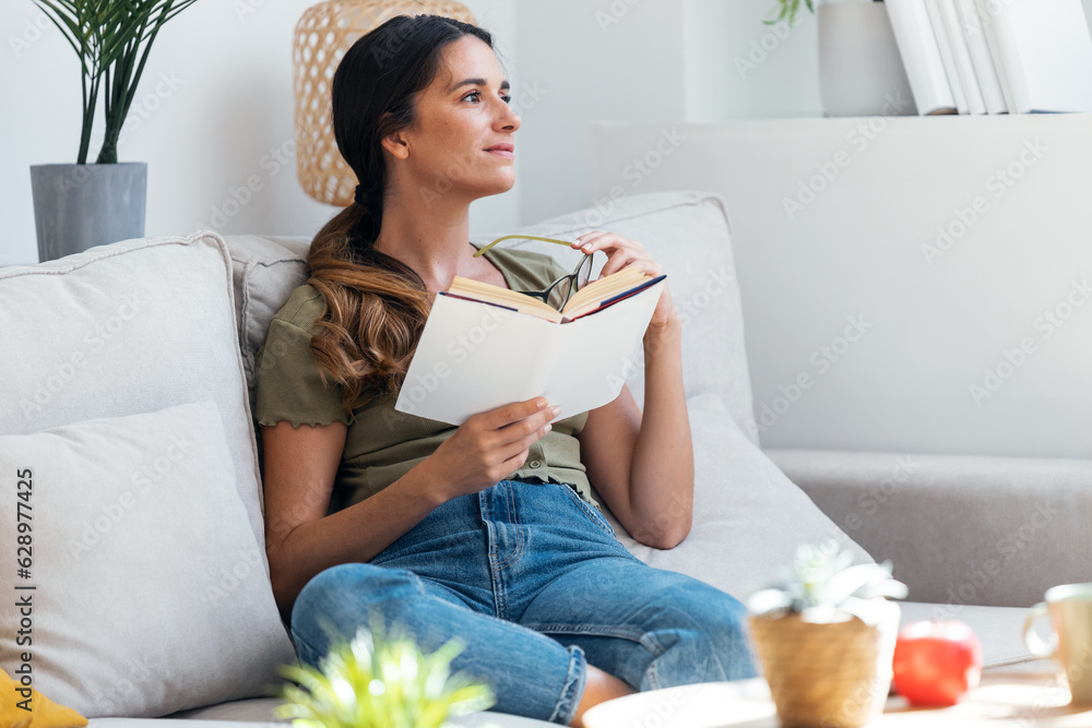 Confident woman reading a book while sitting on sofa at home.