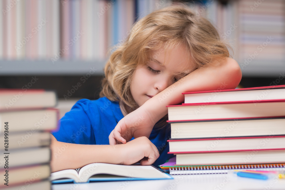 Tired and bored school boy. Child reads books in the library. Schoolkid with book in school library. Kids literature for reading. Learning from books. School education and clever talented pupil genius Tired and bored school boy. Child reads books in the library. Schoolkid with book in school library. Kids literature for reading. Learning from books. School education and clever talented pupil genius